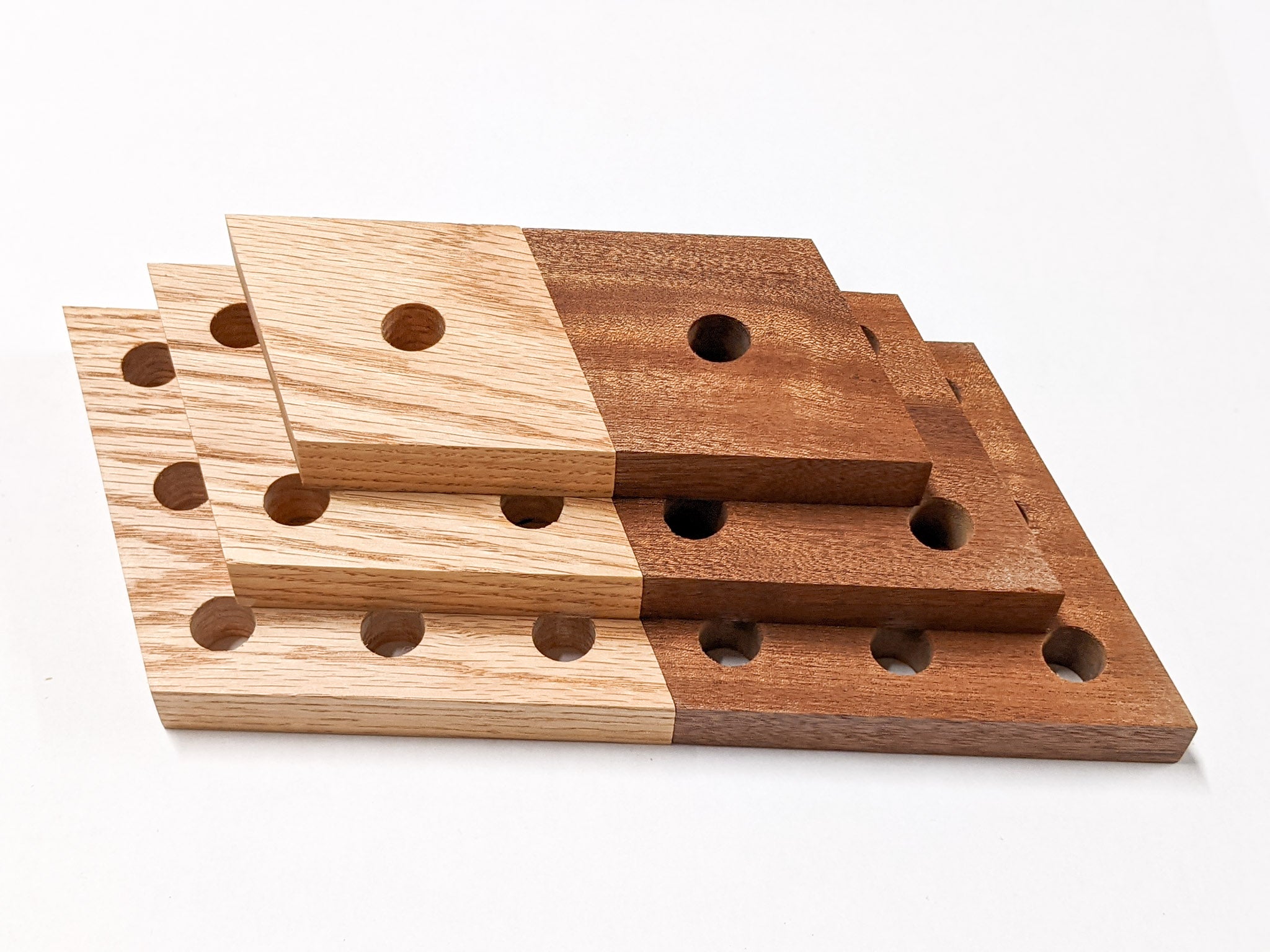 Six rhombus shelves are laid next and on top of each. On the right side, three mahogany rhombus shelves are stacked from largest at the bottom to the smallest propagation shelf at the top. On the left side, three oak rhombus propagation shelves are stacked in a simillar fashion.
